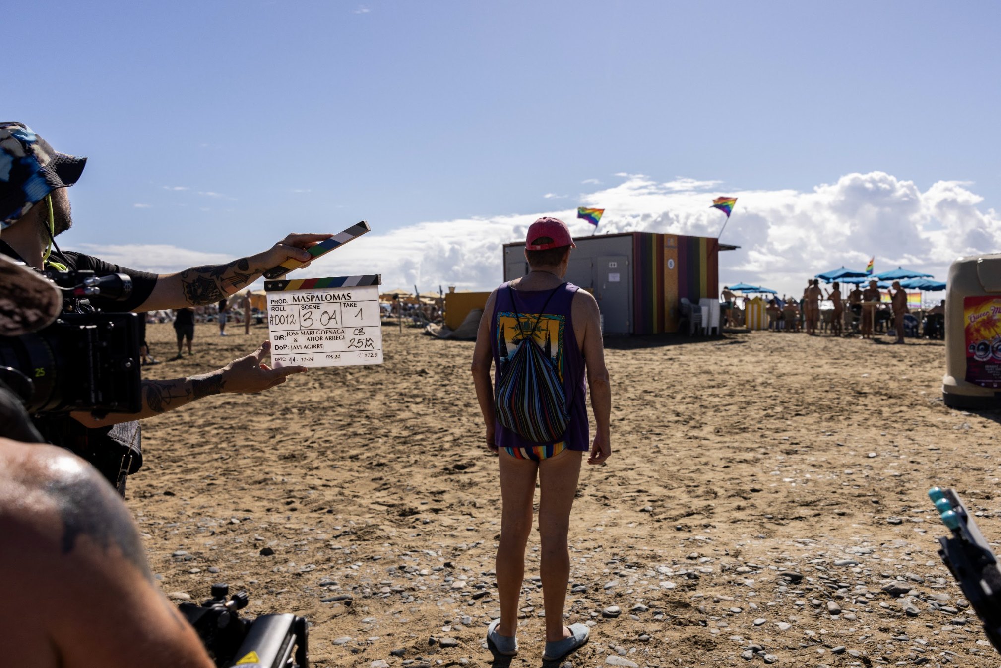 Rodaje de Maspalomas en una playa de Gran Canaria: una claqueta en primer plano y el protagonista, de espaldas, frente a la arena.
