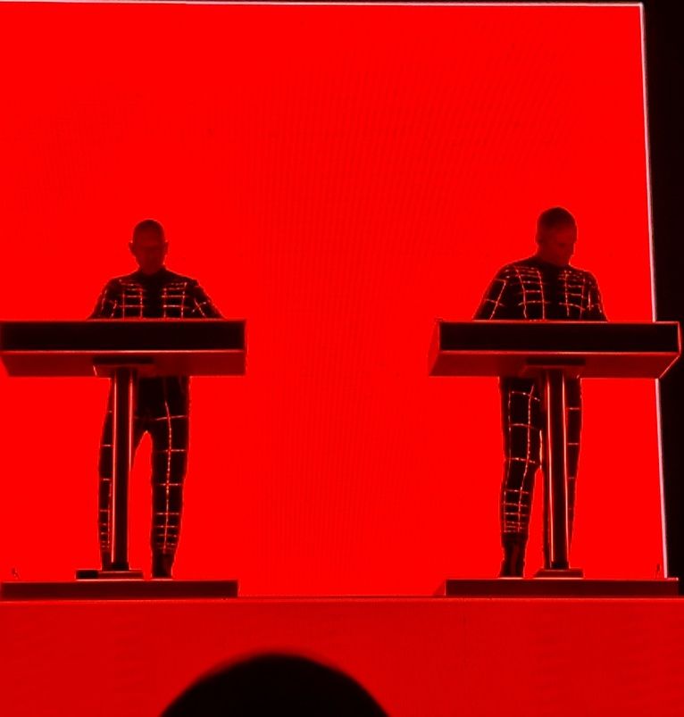 Dos miembros de Kraftwerk, en silueta, ante sus atriles sobre un fondo de luz roja