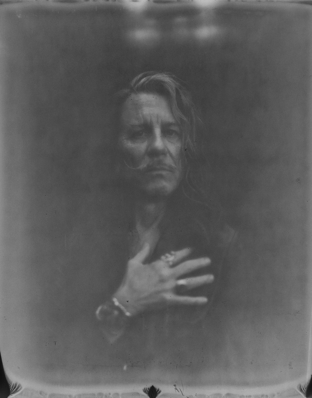 Retrato de William Basinski con la mano sobre el pecho, sobre un fondo gris difuso.